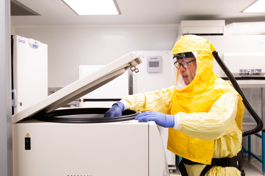 person in yellow hazard suit looking into a grey lab equipment
